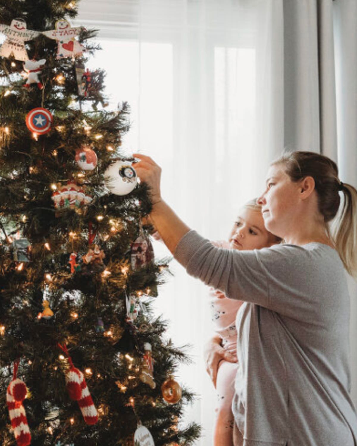 Stacy Canzonieri (mother) and daughter family tradition of hanging ornaments on a christmas tree