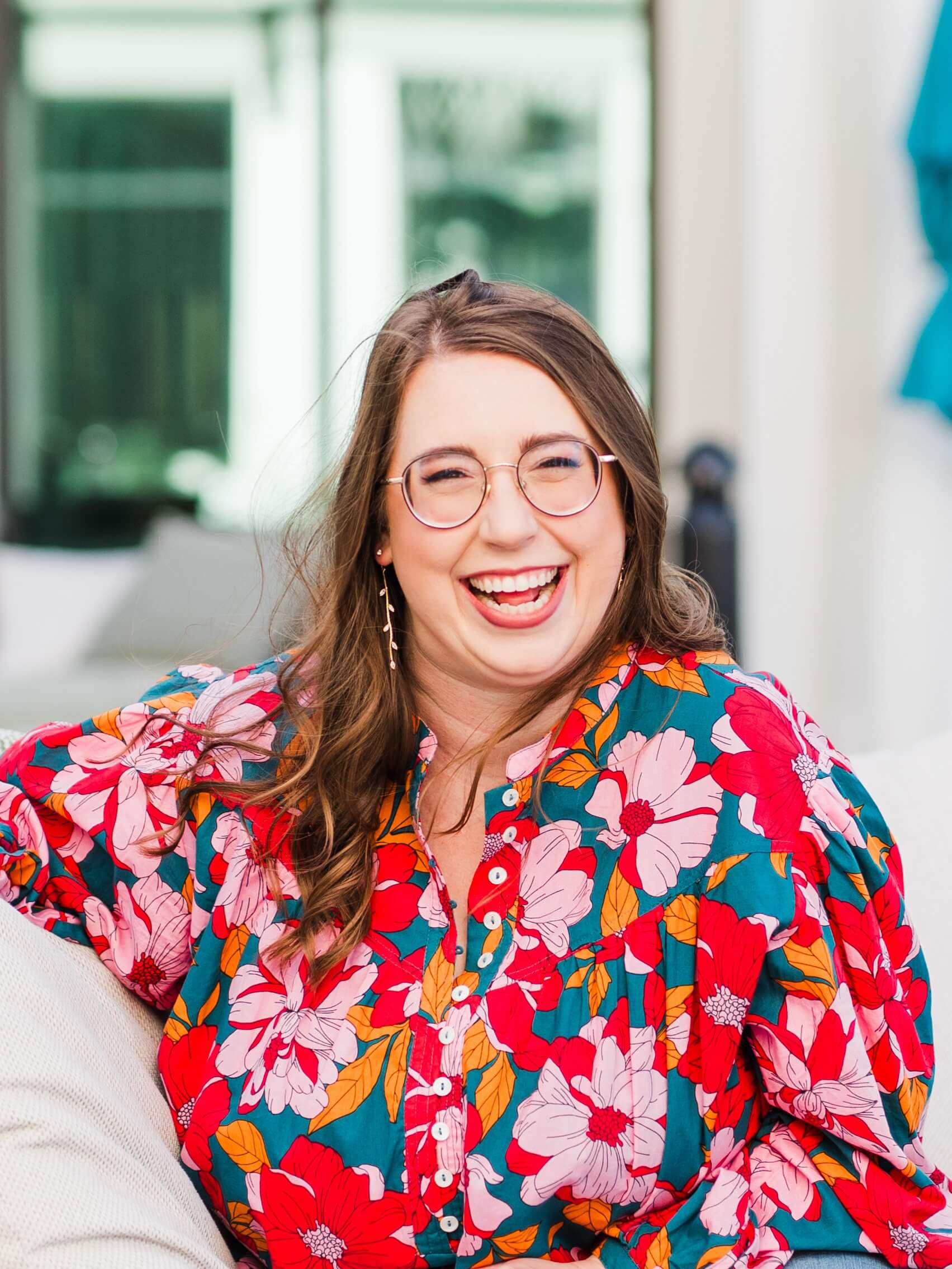 kathryn novak founder of sustainable strategy co smiling on couch wearing a floral pink, red and green shirt.