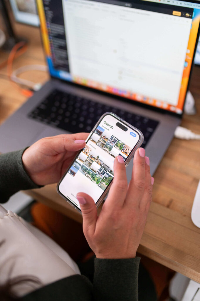 photo management consultant, kiera liu, searches camera roll for photos to organize on iphone with mac laptop in background