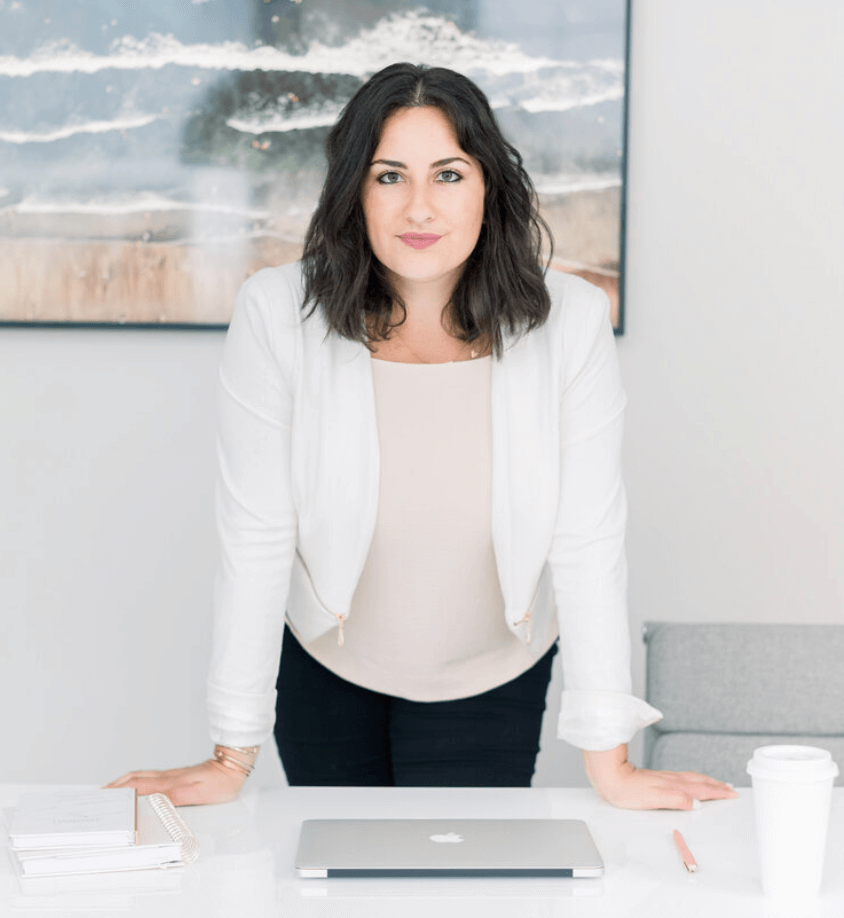 Alessandra Pollina, founder of Quotable Media Co standing at table with closed laptop. female founder power pose