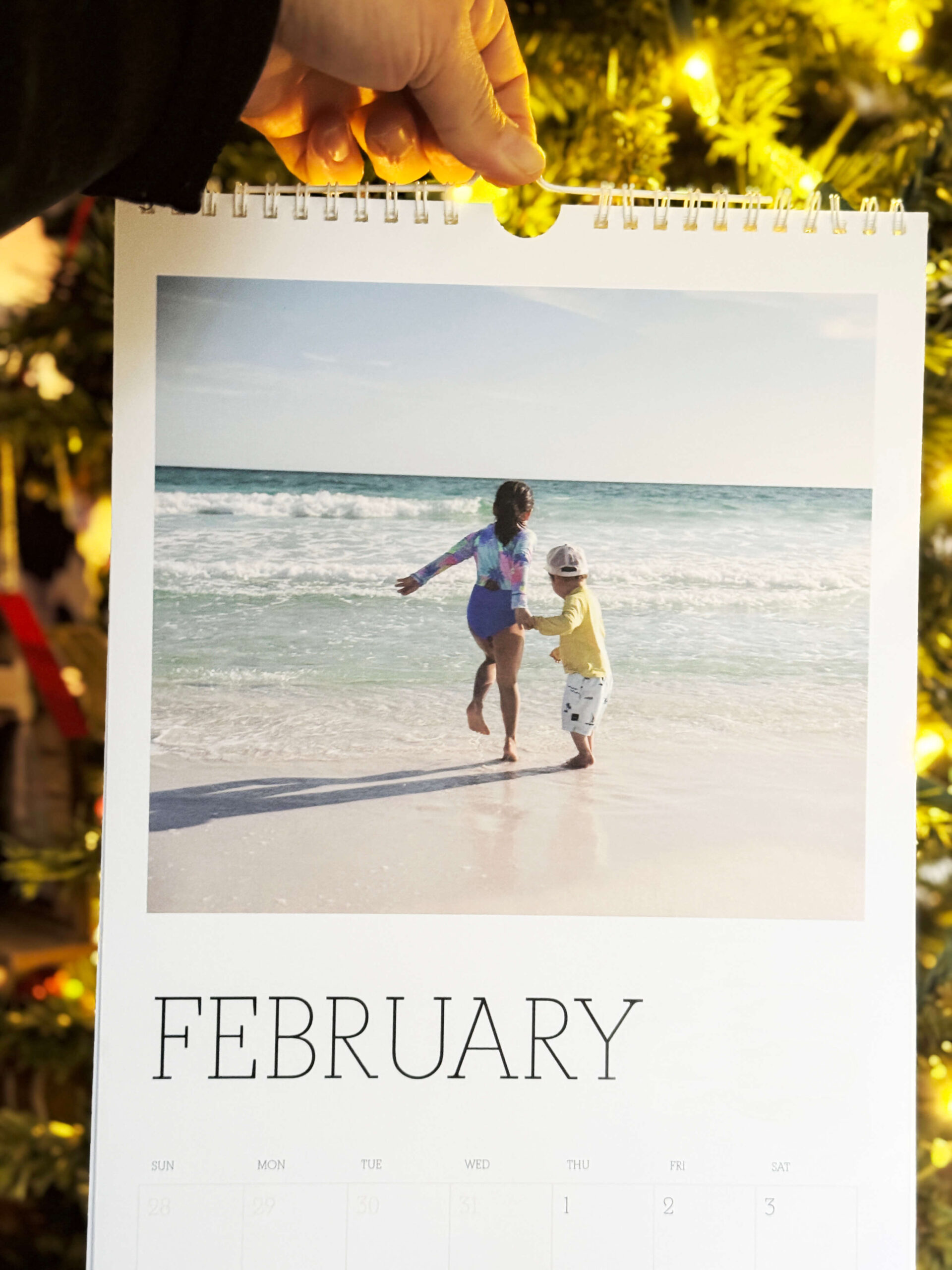 pinhole press large wall photo calendar on February held by hand in front of christmas tree